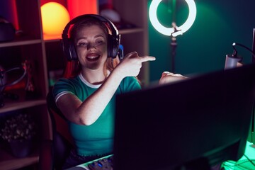 Sticker - Redhead woman playing video games amazed and smiling to the camera while presenting with hand and pointing with finger.