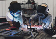 Industrial woman welder teaches younger student how to weld metal with a torch