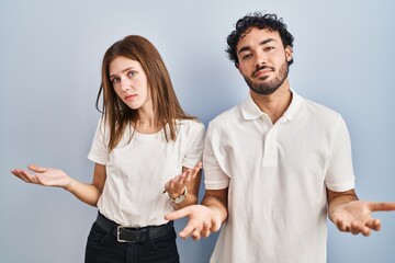 Canvas Print - Young couple wearing casual clothes standing together clueless and confused with open arms, no idea concept.