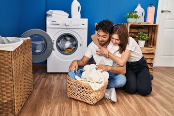 Poster - Man and woman couple hugging each other washing clothes at laundry room