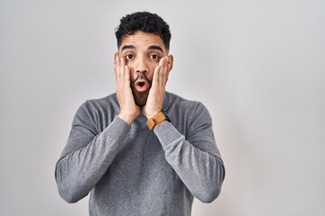 Poster - Hispanic man with beard standing over white background afraid and shocked, surprise and amazed expression with hands on face