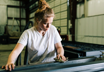 Woman welder working in construction and manufacturing cleans steel metal with a cloth with dirty hands