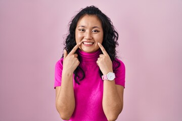 Poster - Young asian woman standing over pink background smiling with open mouth, fingers pointing and forcing cheerful smile