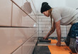 © Kyta Willets - a female trades worker lays tile in a bathroom remodel