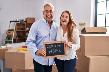 Poster - Middle age hispanic couple moving to a new home holding banner smiling and laughing hard out loud because funny crazy joke.