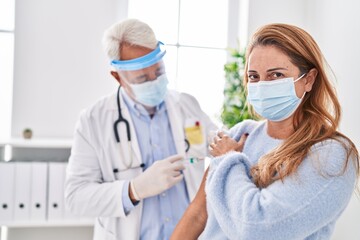 Canvas Print - Middle age man and woman doctor wearing medical mask vaccinating patient at clinic