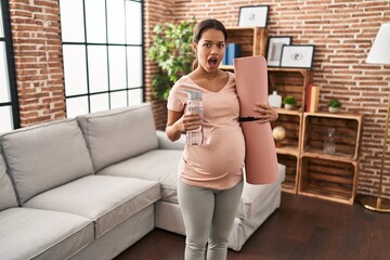 Sticker - Young pregnant woman holding yoga mat at home afraid and shocked with surprise and amazed expression, fear and excited face.