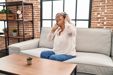 Sticker - Middle age woman listening to music sitting on sofa at home