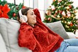 © Krakenimages.com - Young hispanic girl listening to music sitting on the sofa by christmas tree at home.