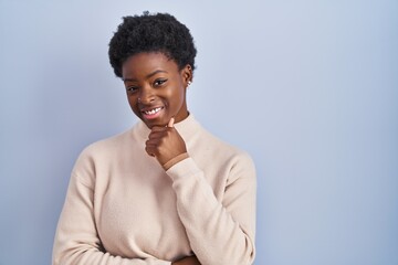 Sticker - African american woman standing over blue background looking confident at the camera smiling with crossed arms and hand raised on chin. thinking positive.