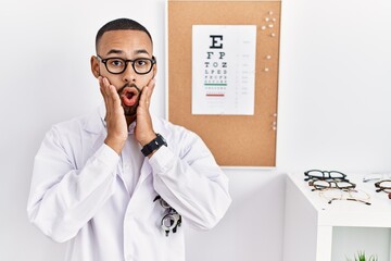 Poster - African american optician man standing by eyesight test afraid and shocked, surprise and amazed expression with hands on face