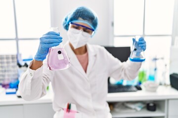 Wall Mural - Young latin woman wearing scientist uniform holding test tubes at laboratory