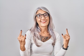 Poster - Middle age woman with grey hair standing over white background shouting with crazy expression doing rock symbol with hands up. music star. heavy music concept.