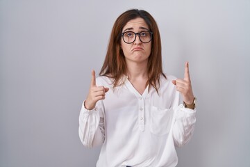 Poster - Brunette woman standing over white isolated background pointing up looking sad and upset, indicating direction with fingers, unhappy and depressed.