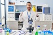 © Krakenimages.com - Young hispanic man with beard working at scientist laboratory excited for success with arms raised and eyes closed celebrating victory smiling. winner concept.