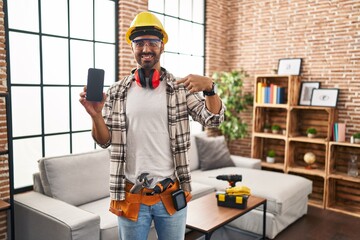 Poster - Young hispanic man with beard working at home renovation holding smartphone pointing finger to one self smiling happy and proud