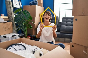 Poster - Brunette woman sitting on the floor at new home holding ruler angry and mad screaming frustrated and furious, shouting with anger looking up.