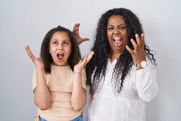 Poster - Mother and young daughter standing over white background crazy and mad shouting and yelling with aggressive expression and arms raised. frustration concept.