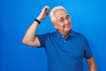 Canvas Print - Middle age man with grey hair standing over blue background confuse and wonder about question. uncertain with doubt, thinking with hand on head. pensive concept.