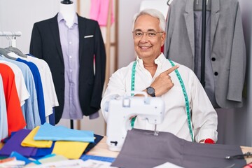 Wall Mural - Middle age man with grey hair dressmaker using sewing machine cheerful with a smile on face pointing with hand and finger up to the side with happy and natural expression