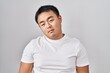 © Krakenimages.com - Young chinese man standing over white background looking sleepy and tired, exhausted for fatigue and hangover, lazy eyes in the morning.