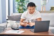 © Krakenimages.com - Young chinese man counting dollars sitting on sofa at home