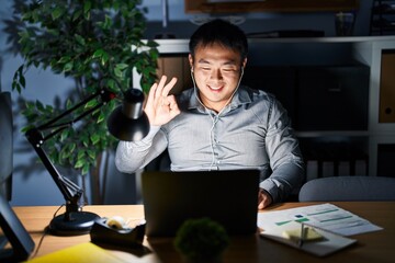 Canvas Print - Young chinese man working using computer laptop at night showing and pointing up with fingers number three while smiling confident and happy.