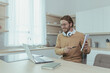 © Liubomir - Young teacher teaches remotely from home, man works in kitchen at home, uses laptop for online call with communicates with students smiling explains assignment shows notebook.
