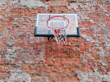 Old And Worn Outdoor Basketball Hoop Net On The Red Brick Wall Background, Urban Playground, Downtown In The City