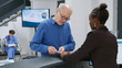 © DC Studio - Senior man paying with credit card at hospital reception desk, making electronic payment transaction for medical checkup appointment and treatment. Receptionist helping man to pay.