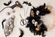 DIY Halloween Wreath Background. Process Of Making Wreath With Glue Gun, Black Feathers, Skulls And Golden Leaves
