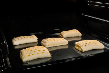 Five puff pastry buns with fruit jam baking and rising on tray in electric oven. Homemade bakery, food, cooking and pastry concept