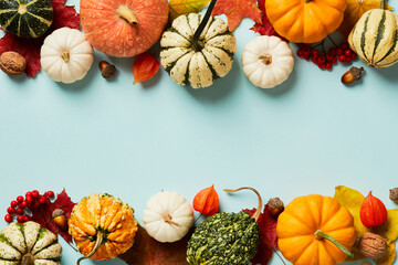 Autumn frame. Different decorative pumpkins, autumnal decorations, maple leaves, acorns, rowan branches, physalis on pastel blue table. Flat lay, top view, copy space.