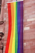 Rainbow LGBT Flag Handing Down By The Catholic Church Of The Holy Spirit In The Center Of Heidelberg, Germany. Brick Wall On The Background