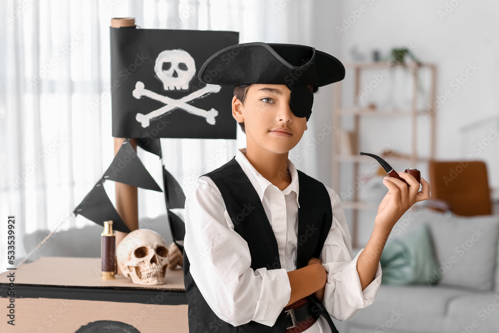 Little boy dressed as pirate with smoking pipe and cardboard ship at home