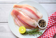 fresh raw pangasius fish fillet with herb and spices lemon lime and rosemary, meat dolly fish tilapia striped catfish, fish fillet on white plate with ingredients for cooking - top view