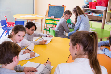 Wall Mural - Group of school kids with pens and notebooks studying in classroom with teacher