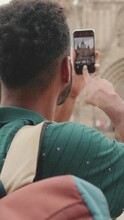 VERTICAL VIDEO: Young Man Tourist Takes Photo On Cellphone While Standing On The Square Of The Old City. Back View