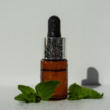 A Bottle With Essential Oil And Mint On A White Background. Essential Aroma Oil. Glass Bottle Of Peppermint Essential Oil With Fresh Green Mint Leaves, Mint Oil. Selective Focus. 