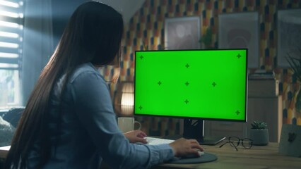 Poster - Asian woman sitting at the table and looking at screen of personal computer while working remotely from home or browsing the internet in free time. Freelance. Green screen and chromakey