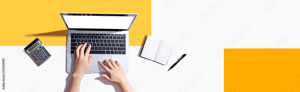 Person using a laptop computer with a notebook and a calculator
