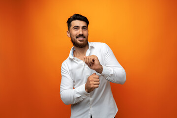 Wall Mural - Young man celebrating and dancing against orange background in studio