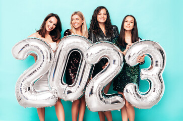 Beautiful women celebrating New Year. Happy gorgeous female in stylish sexy party dresses holding silver 2023 balloons, having fun at New Year's Eve Party. holiday celebration. Charming models