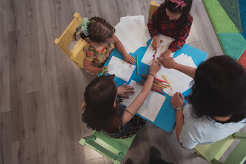 Wall Mural - Creative kids during an art class in a daycare center or elementary school classroom drawing with female teacher. 