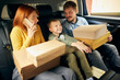 © master1305 - Young happy family, parents and kid sitting at car with a lot of carton boxes after shoopping day, going home. Black Friday or cyber Monday