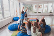 © .shock - A happy female teacher sitting and playing hand games with a group of little schoolchildren