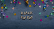 © Alina - Banner with Black Friday text and holiday tinsel flat lay on dark background.