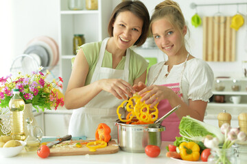 Wall Mural - Beautiful girl with her mother preparing a salad in the kitchen