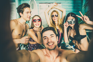 Wall Mural - Group of five friends celebrating in their summer beach house. Party people spending a vacation day in their bungalow in a tropical village in front the ocean