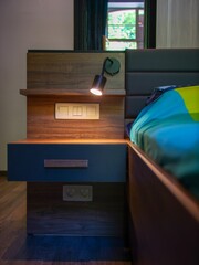 Sticker - Vertical shot of a wooden bedside table with an illuminated lamp and black drawers